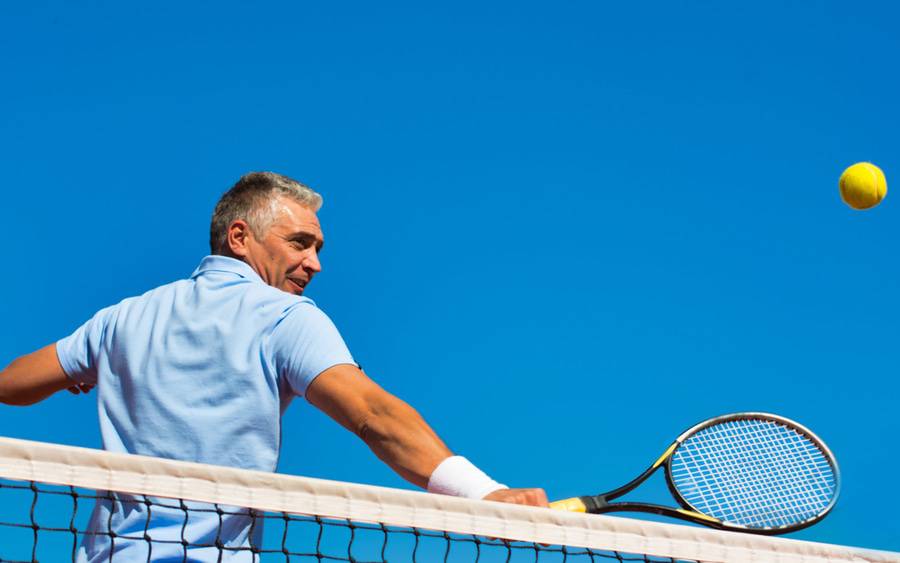 An older man with gray hair hits a tennis ball over the net.