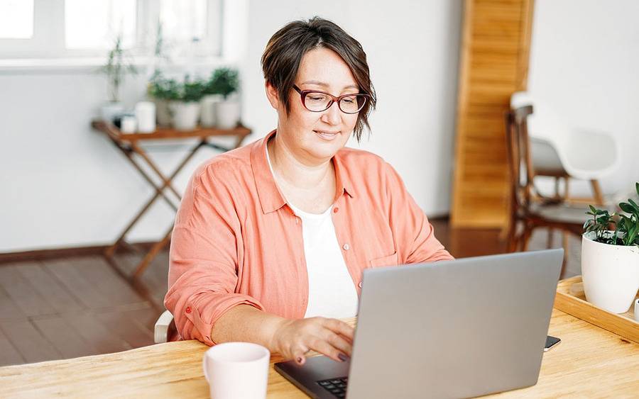 A middle-aged woman types on her laptop at home, representing a virtual support group.