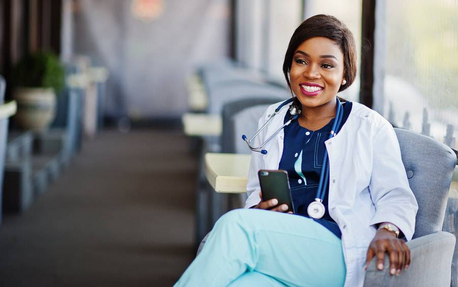 A young woman wearing a white doctor's coat smiles as she holds her phone to make an order for the Colors Cafe at Scripps in San Diego.