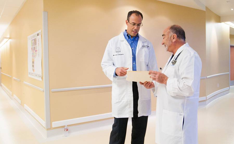 Two male cardiologists confer patient notes in in a hospital hallway as part of the Scripps Kaiser Permanente partnership.