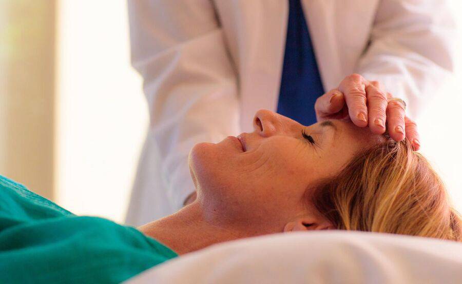A female patient laying down receiving a holistic treatment from a physician.