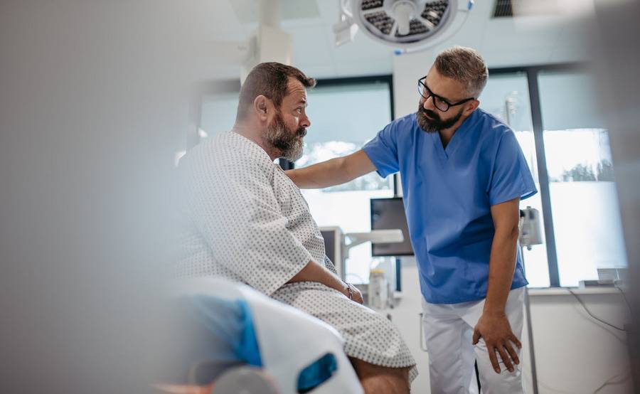 A doctor places a comforting hand on a patient's shoulder in a hospital room, representing interventional pulmonology.
