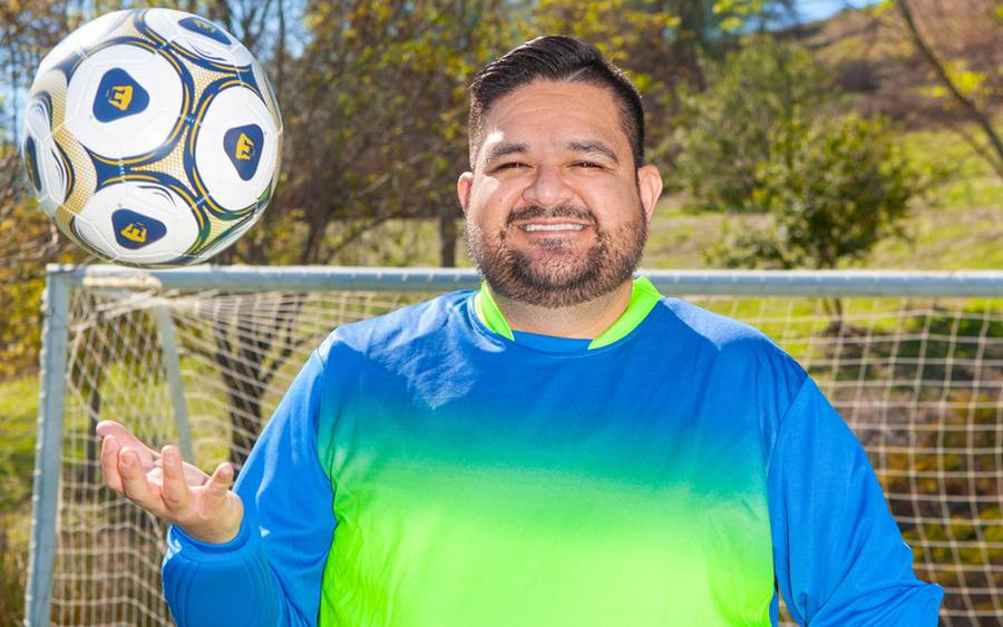 Juan Ramos tosses a soccer ball in his hand in front of a soccer goal post.
