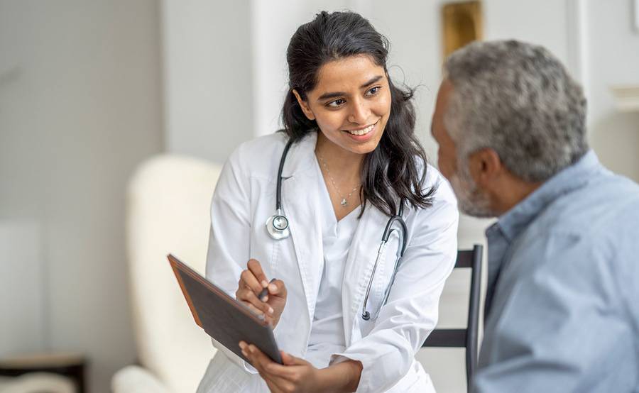 A kind young female provider speaking and documenting their conversation with a male patient in a clinical setting.
