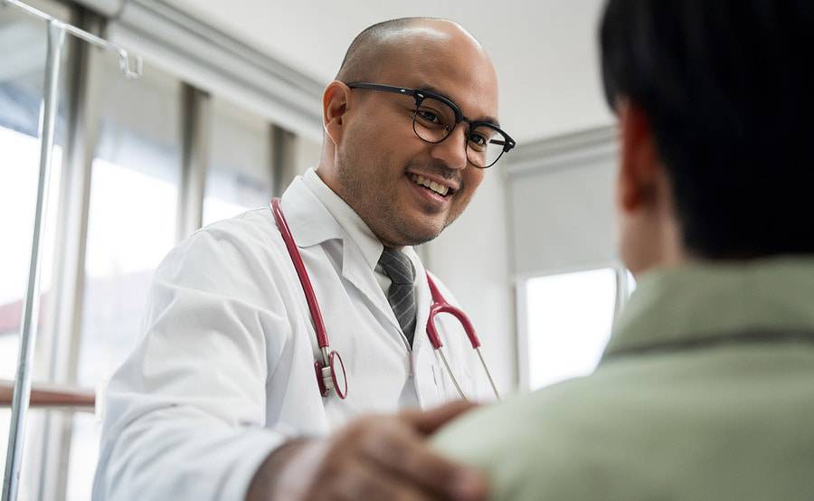 A male provider focused on and caring for the male patient as he smiles at his patient while discussing his care.