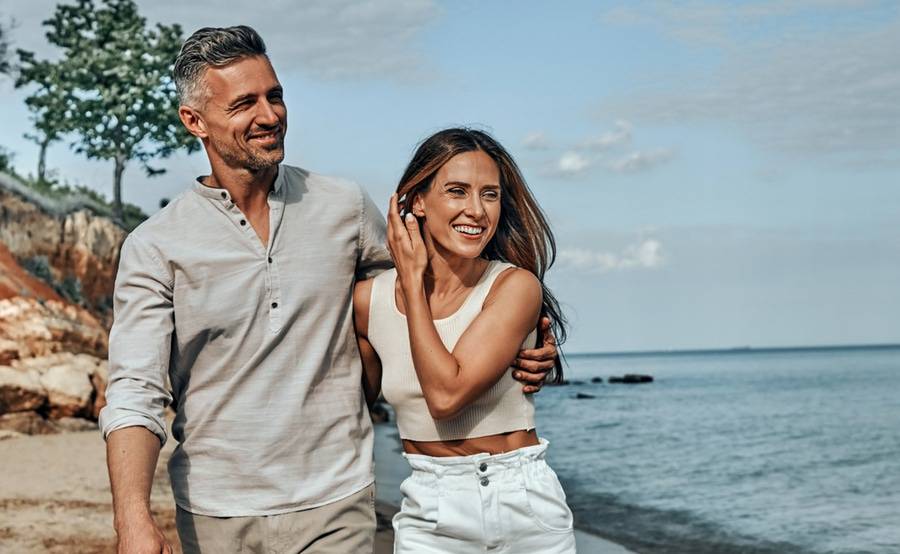 Mature couple walking on the beach, smiling and standing close to each other.