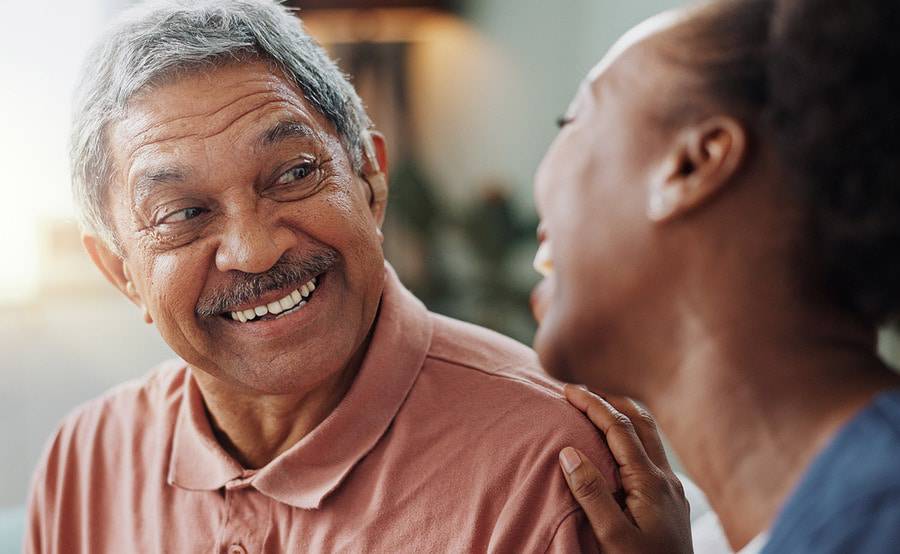 An older male patient smiling and engaging with the female provider to his right as they discuss his care.
