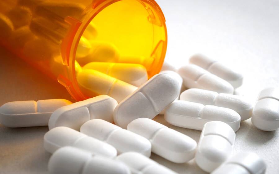 A bottle of opioid pills is opened and spilled out on a table.