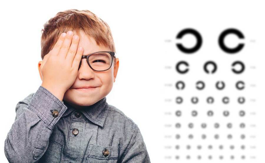 A child in front of an eye chart with a hand over his eye illustrating pediatric eye care at Scripps.