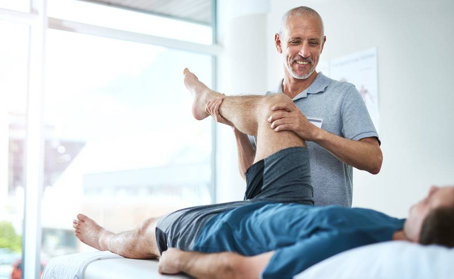 A physical therapy expert provides care to a reclining patient stretching his leg in a clinical setting.