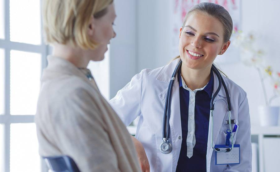 A female provider in a navy blue top smiling while speaking to a patient.