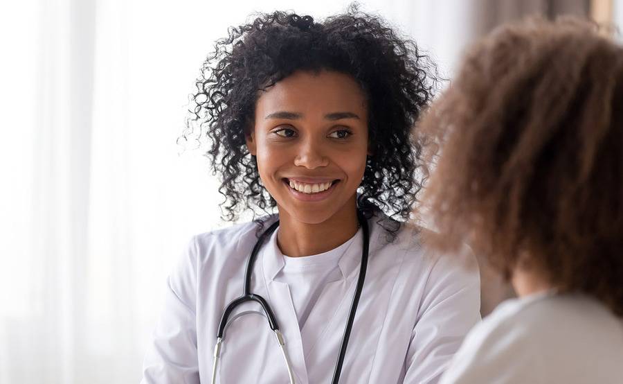 A happy female provider with curly hair smiling while talking to a female patient.