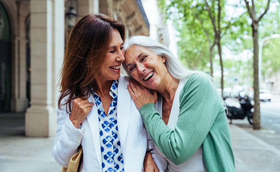 Two middle-aged woman laugh on a city street, representing a fuller life with treatment for renovascular disease.