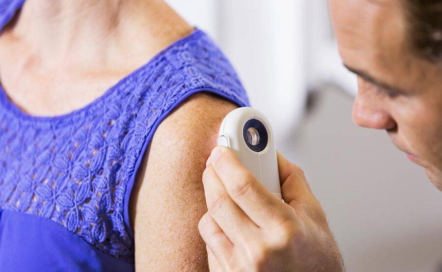A doctor closely examines an area of a patient's skin related to skin cancer diagnosis and staging at Scripps Cancer Center