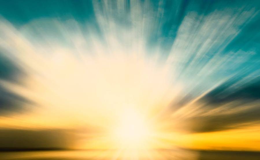 The sun sets over the ocean shining rays of light in all directions.