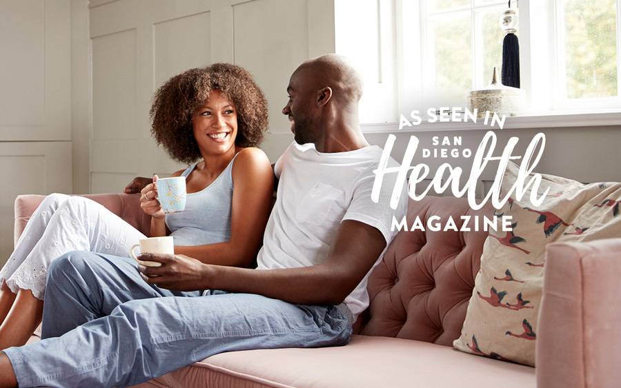 A young black man and woman smile as they sit relaxed on the couch with their feet up.