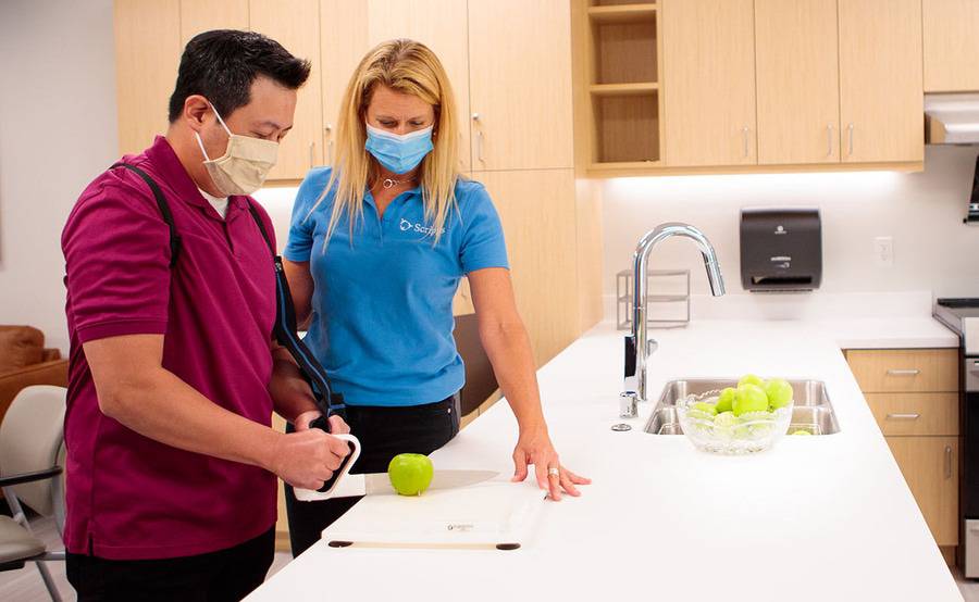 A stroke patient with a therapist working on cooking skill of cutting during a stroke rehab session.