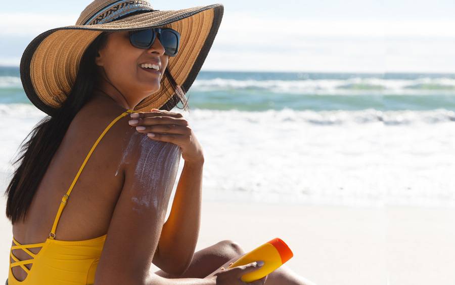 A woman at the beach lathers sunscreen lotion on her arms at the beach.