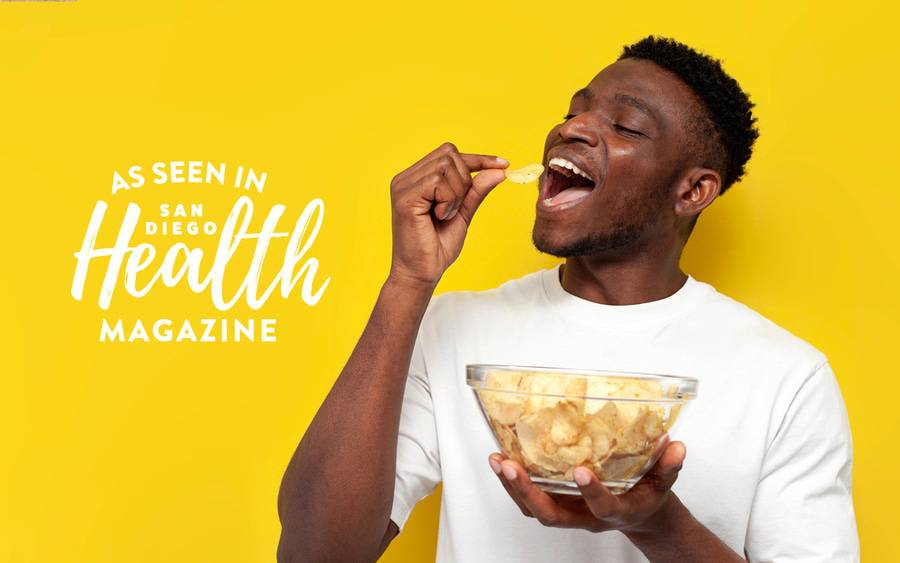 A young black man holds a bowl of chips and is about to put a chip in his mouth.