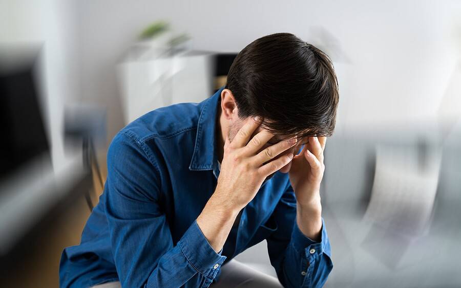 A man sits holding his temples, experiencing dizziness from vertigo.