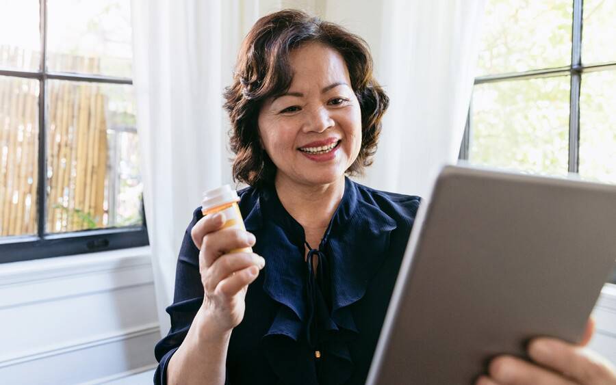 Telemedicine patient using tablet and holding prescription to show her doctor via video.