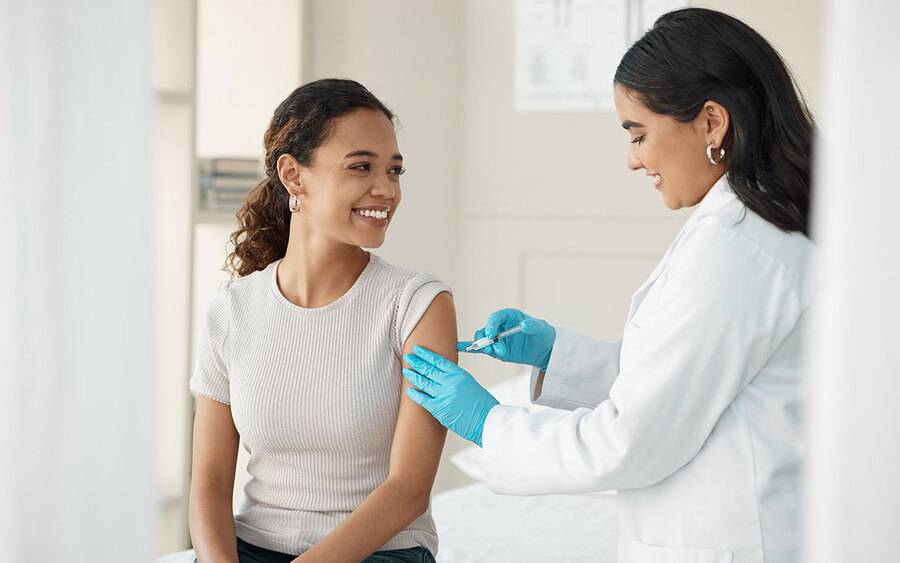 A young woman in a grey shirt receiving a vaccine from a provider illustrates the Flu Season vaccination.