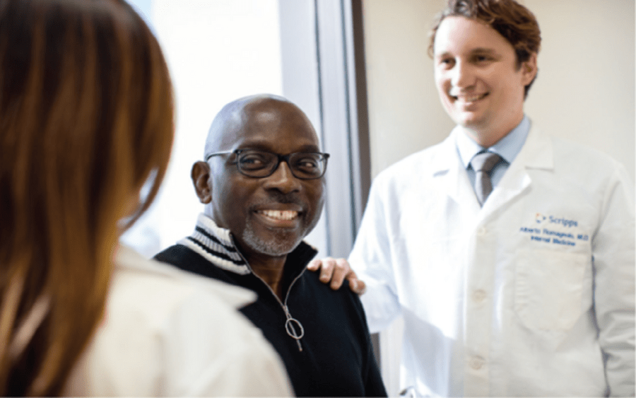 A young white male doctor comforts a black male patient, representing how Scripps Community Benefits expand the GME program.