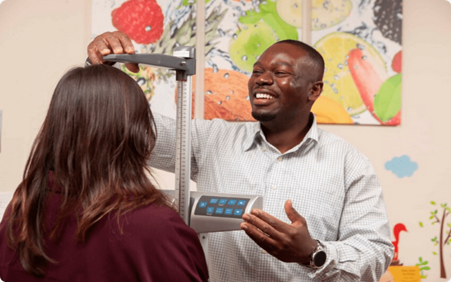 A young black man measures the height of a woman with brown hair, representing how Scripps Community Benefits help families.